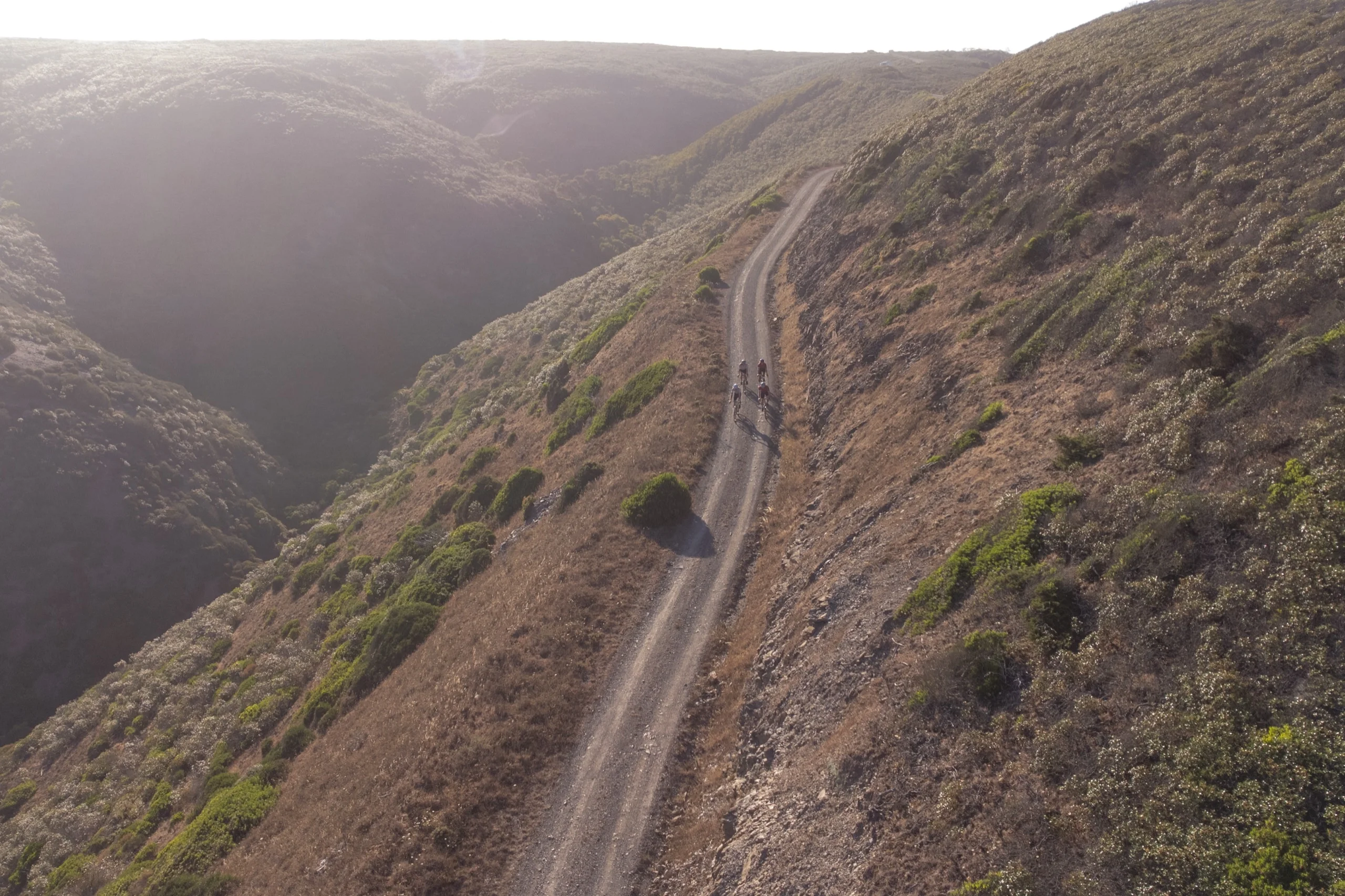 Gravel riders on a track along a steep valley, seen from the air
