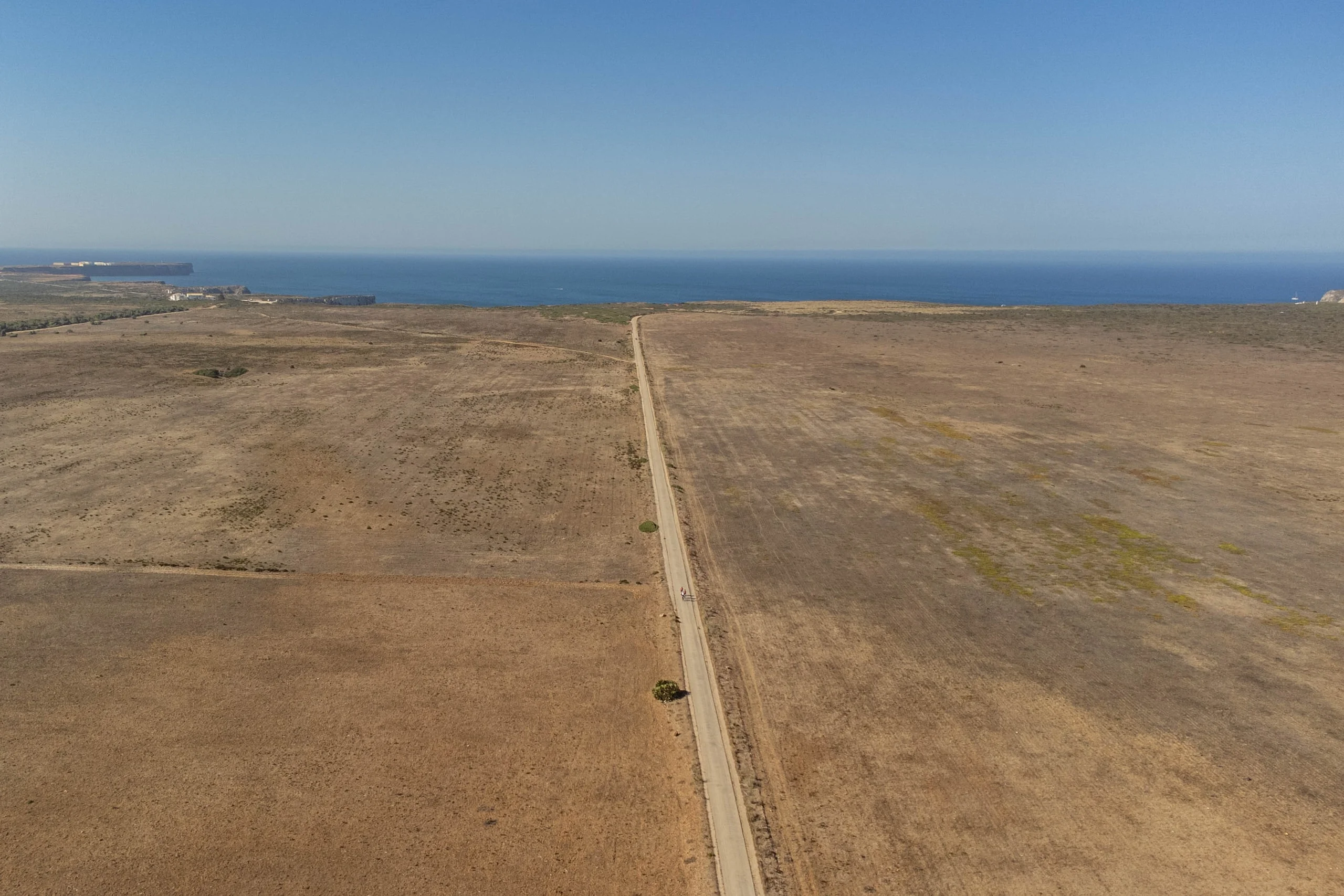 A straight road through dry fields running towards the sea, seen from the air