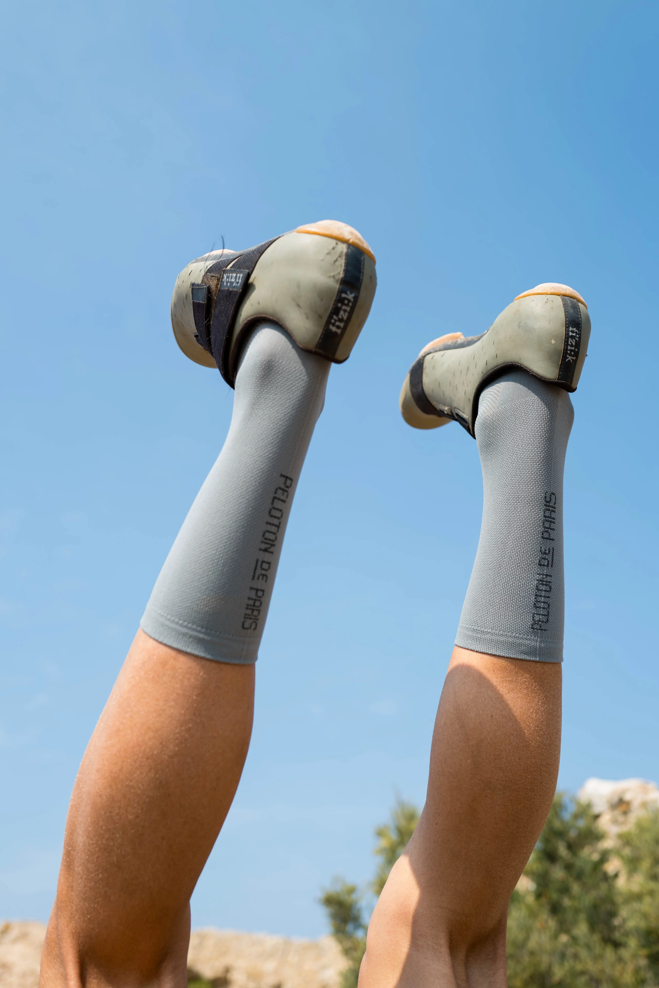 A cyclist's legs in grey cycling socks up in the air against a blue sky, resting after the ride