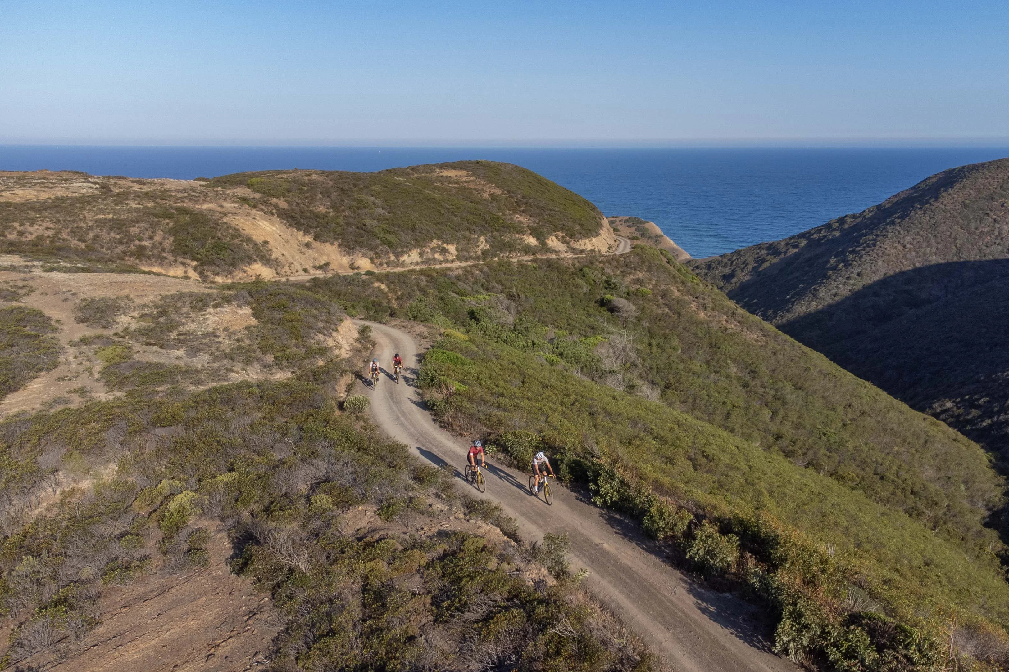 Four riders on a coastal gravel ridge in golden light