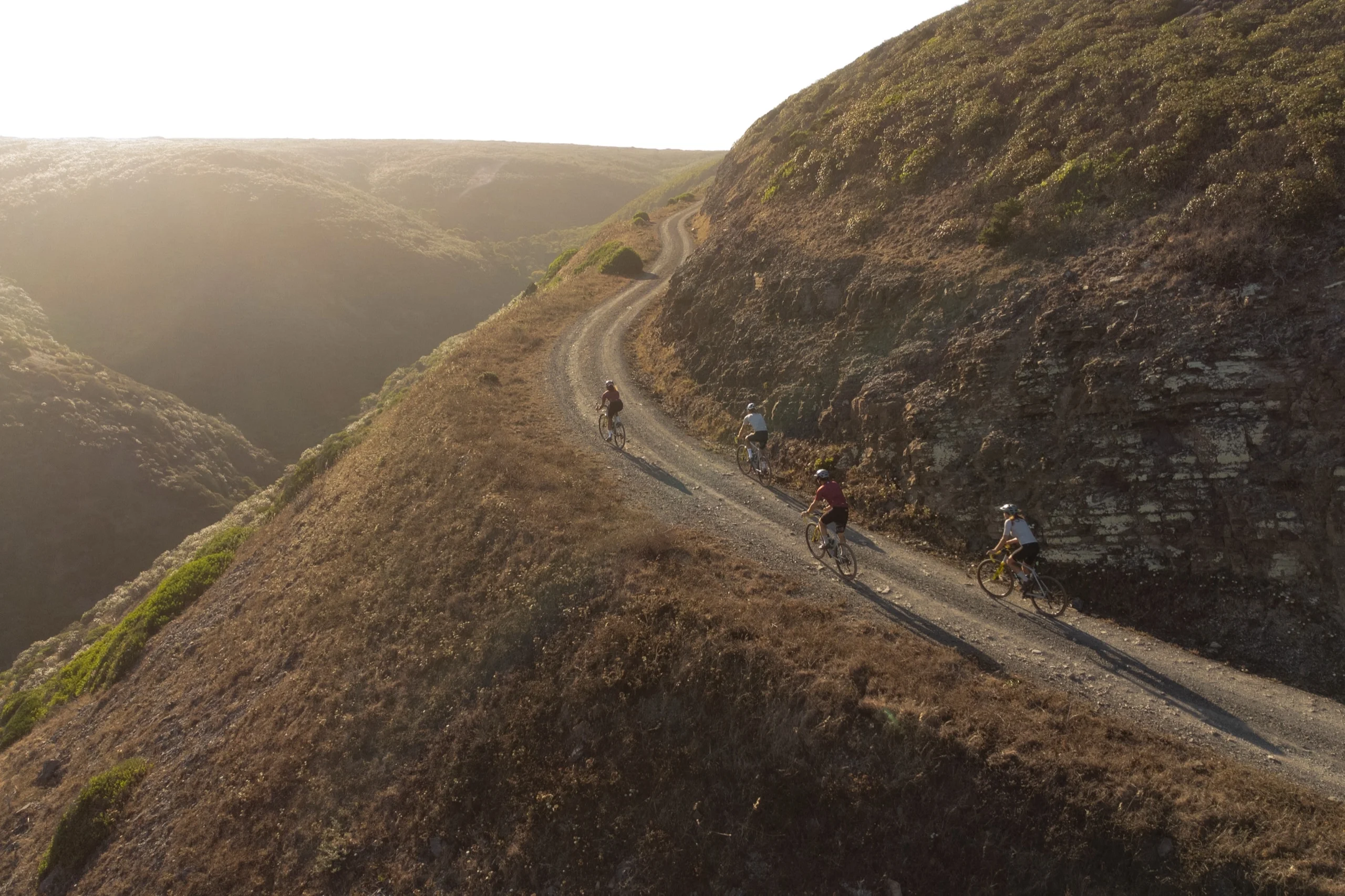 Four riders on a gravel track along a ridge above the valleys of the Costa Vicentina, late afternoon