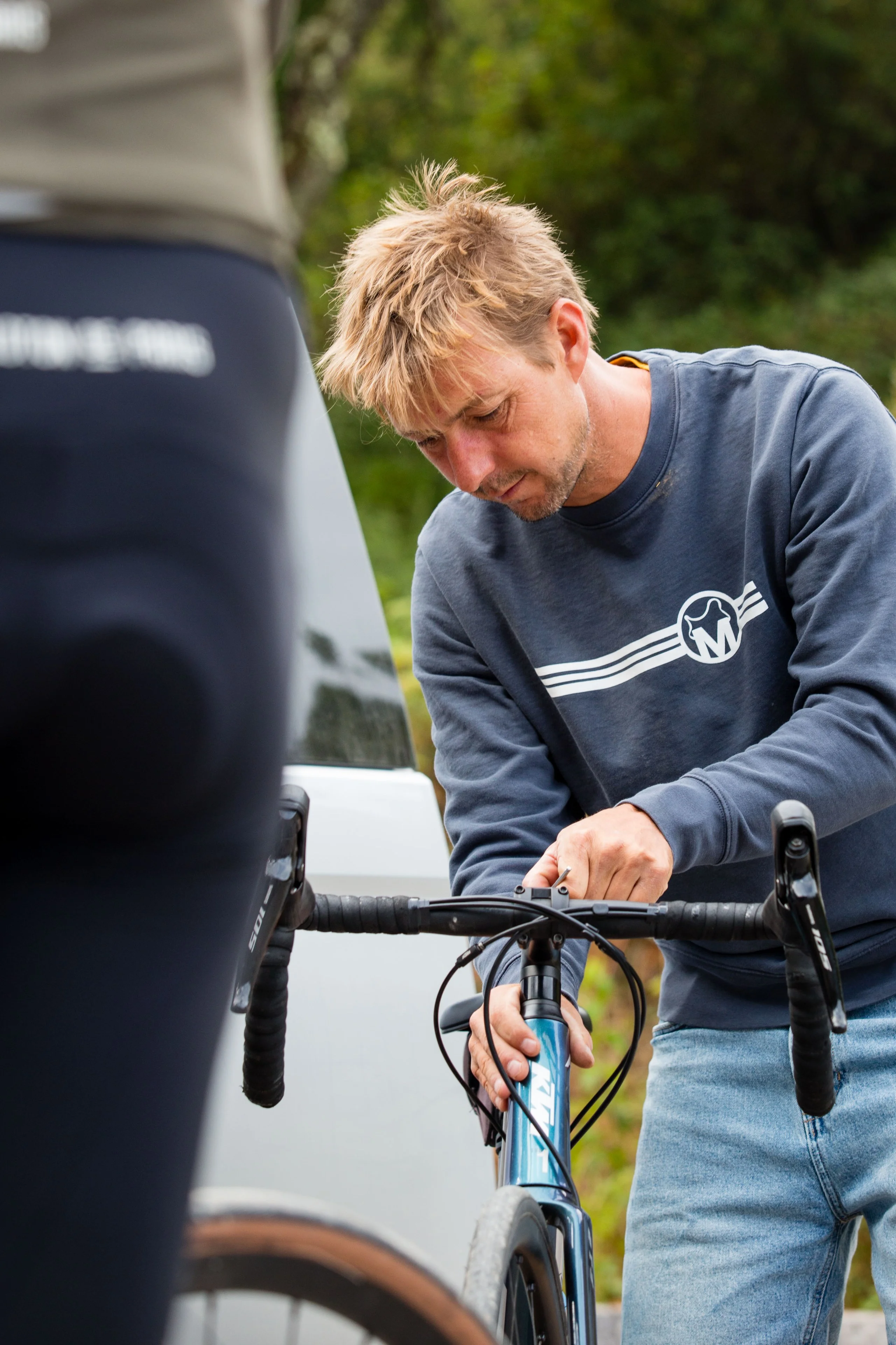 Jerom Pannier, founder of Musette Travel, adjusting the stem of a road bike beside the Musette van