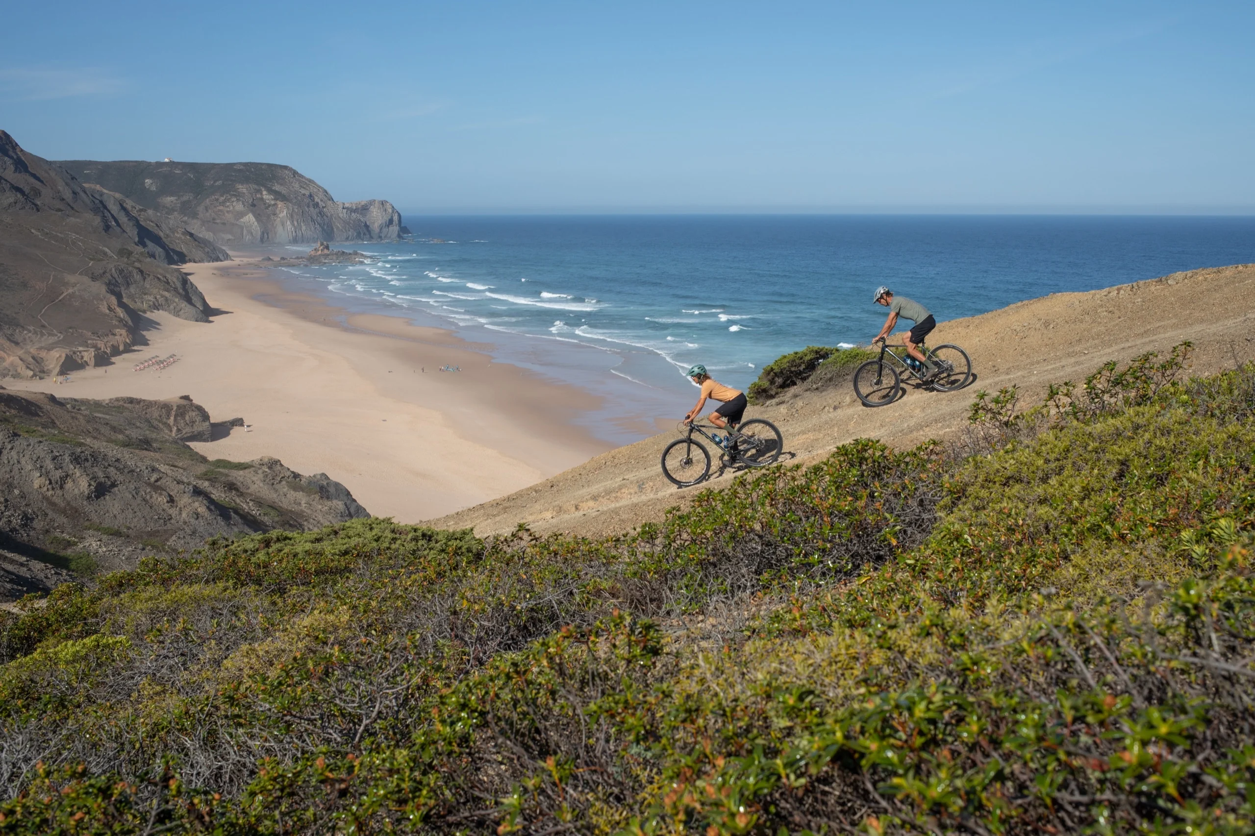 Two mountain bikers on a cliff above a beach in the Costa Vicentina natural park