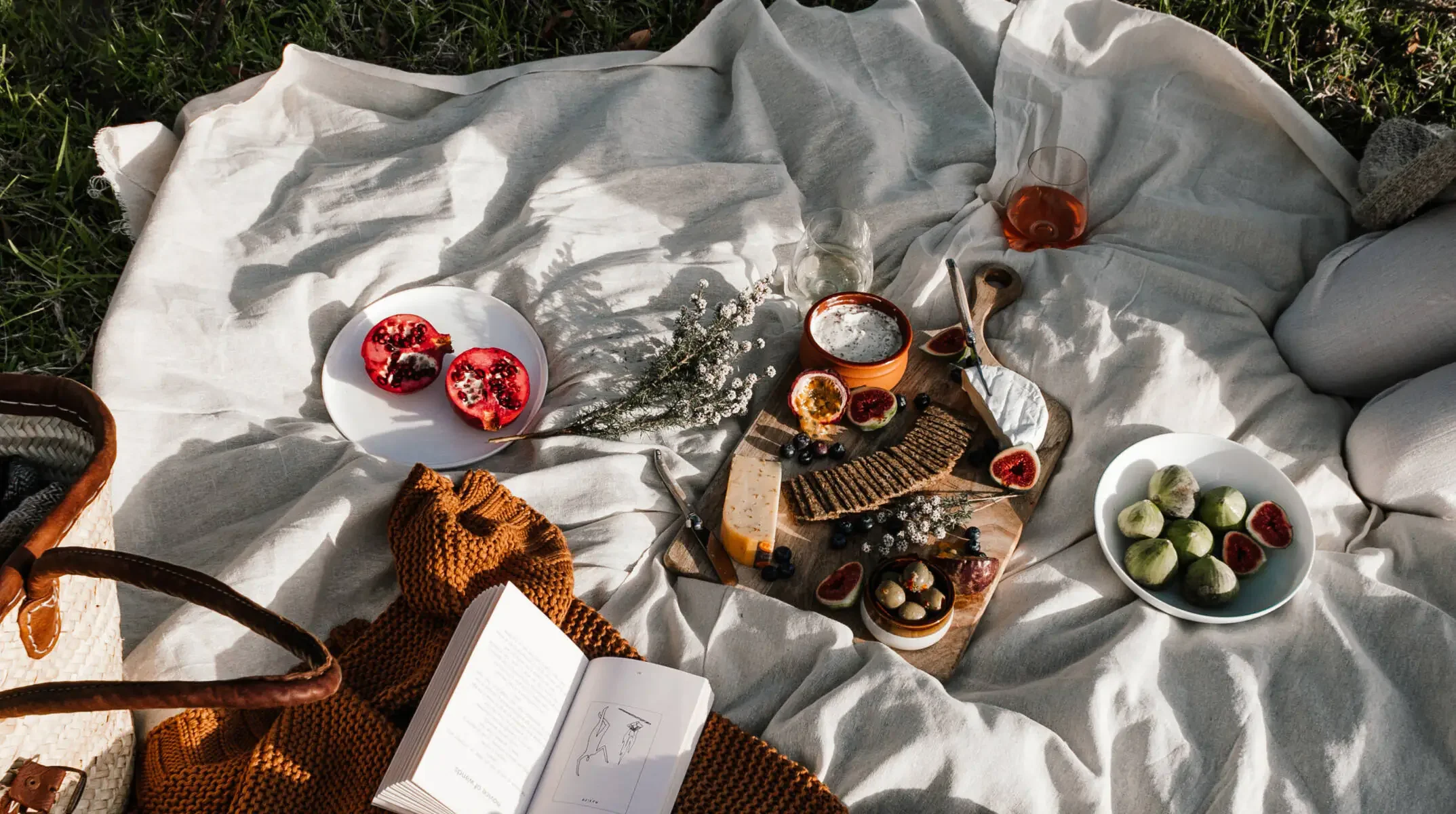 A picnic of figs, pomegranate, cheese and wine on a linen blanket in the grass