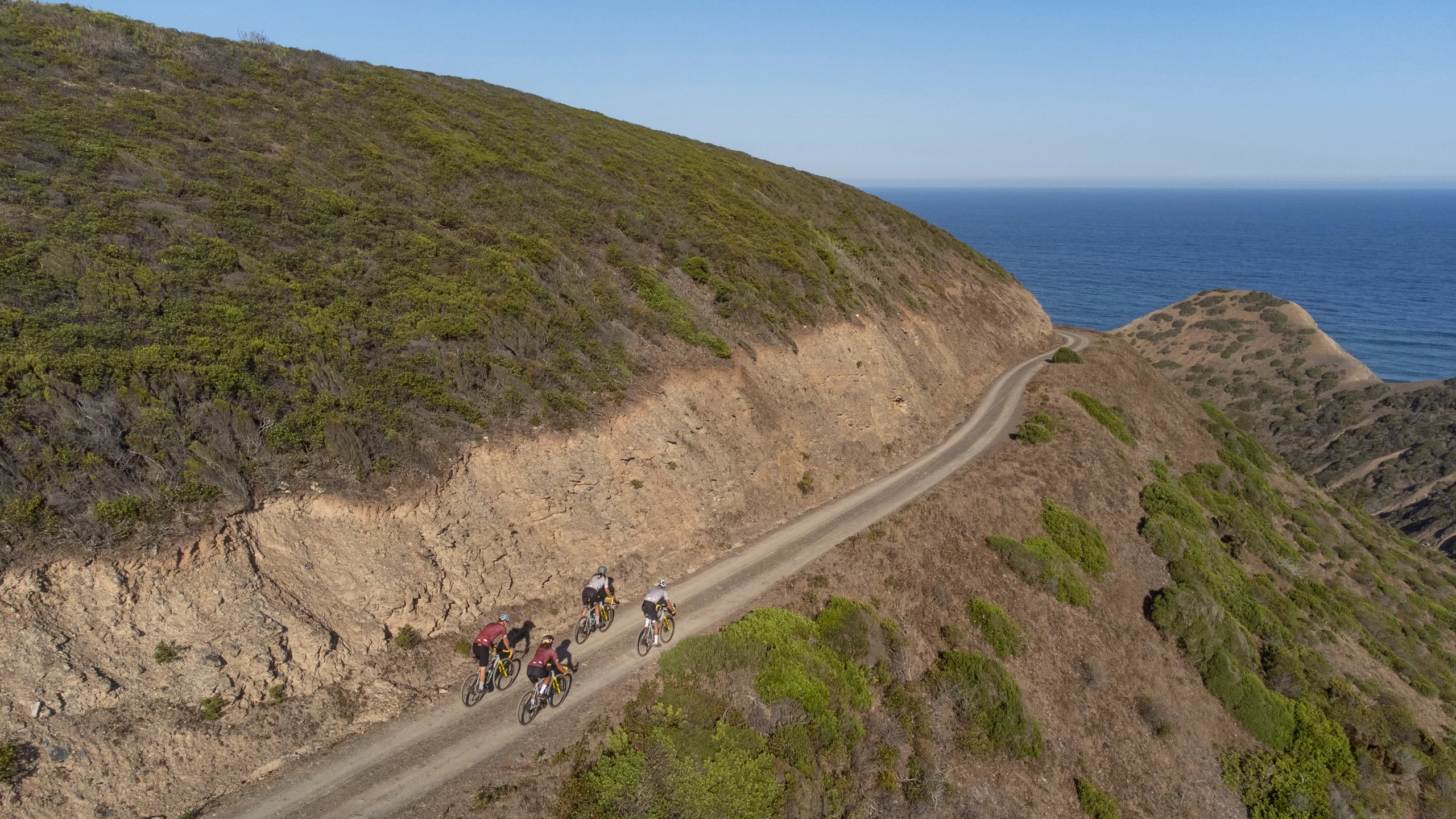 Riders on a gravel track cut into the cliffs above the Atlantic, seen from the air