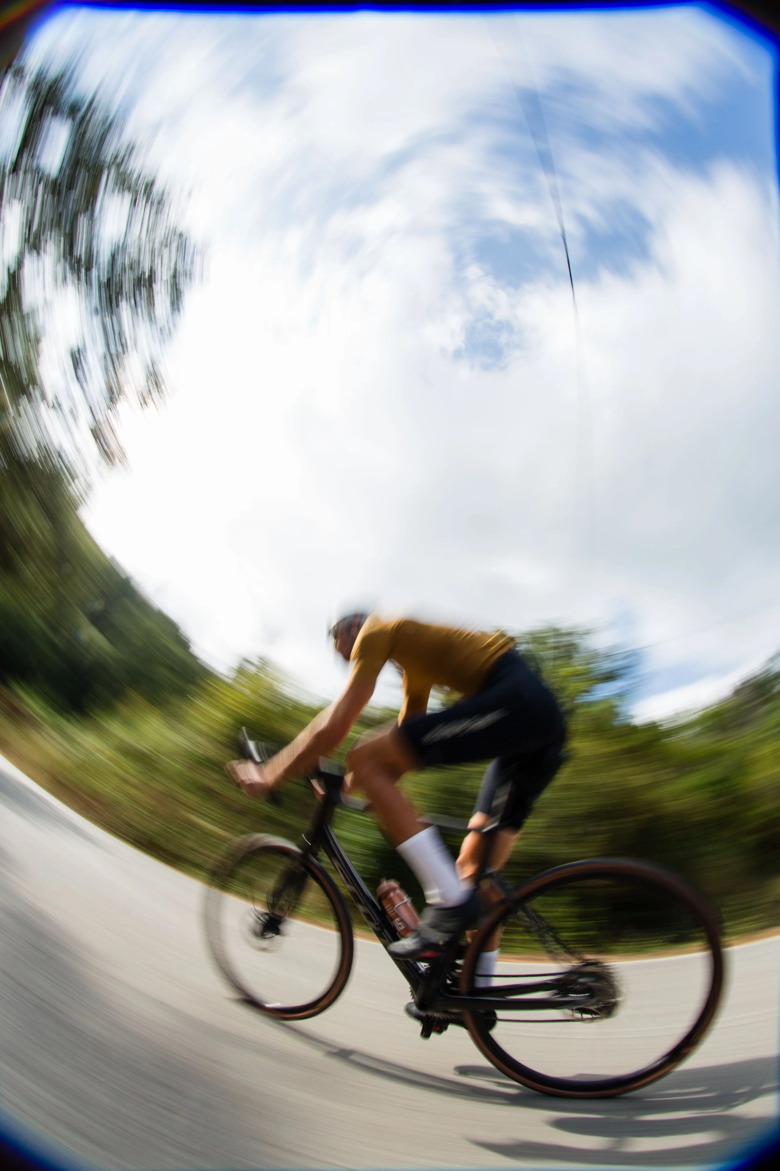 A road cyclist on a carbon road bike riding fast on a quiet road, shot with a fisheye lens
