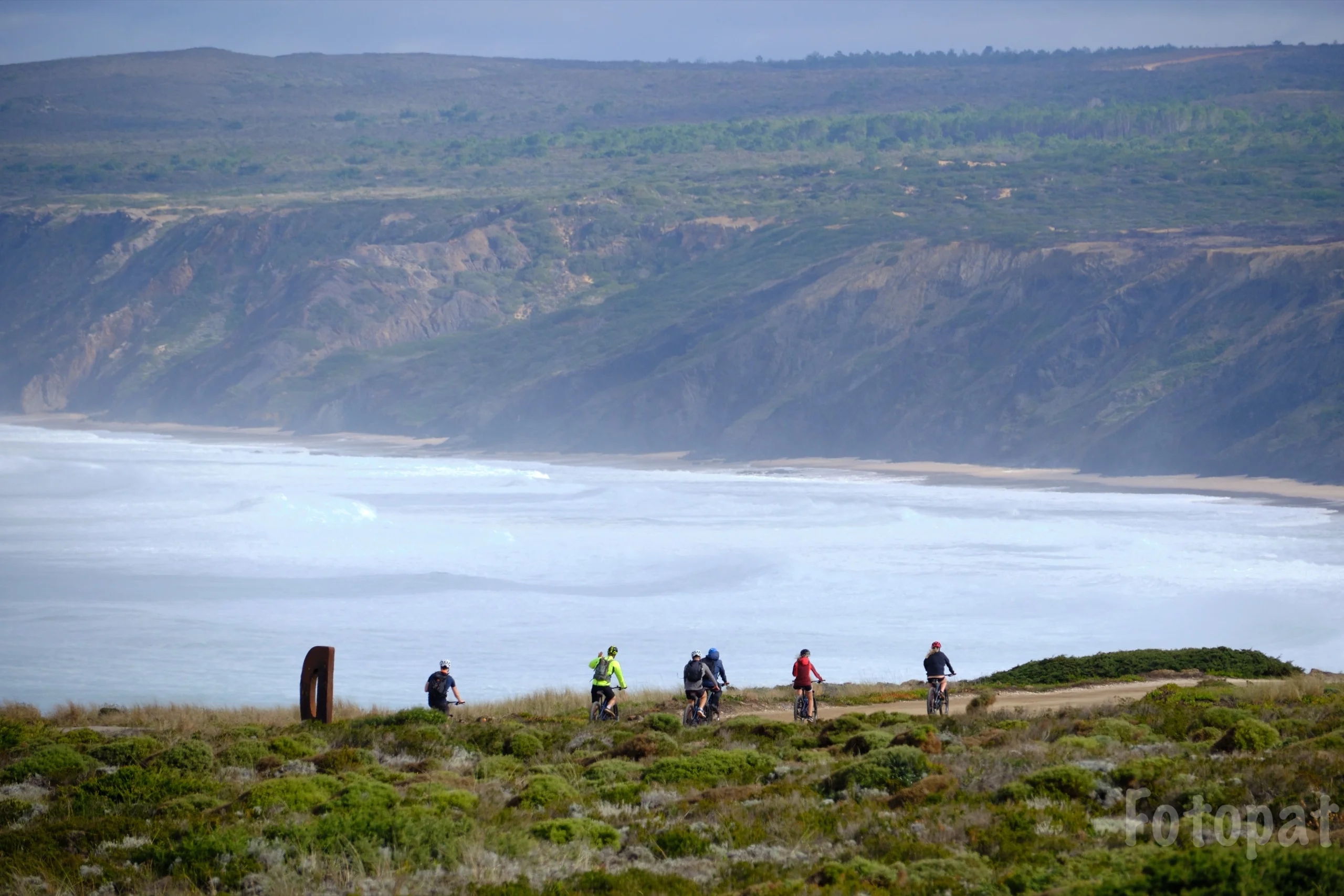 Mountain bikers on the clifftop above a long surf beach in the western Algarve