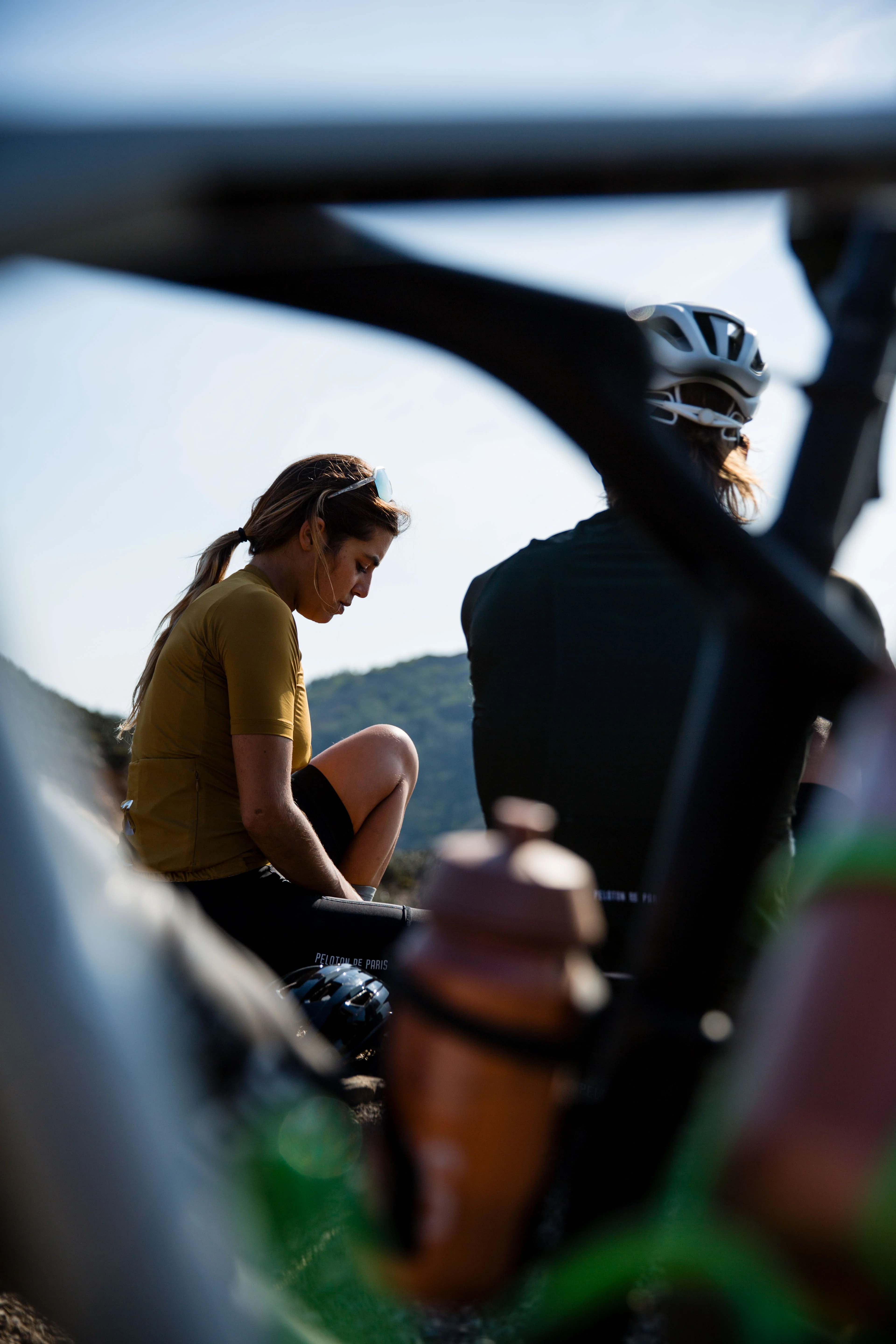 Two women cyclists taking a break on a ride, seen through the frame of a road bike